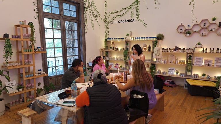 Four people working at a wooden table in a bright craft studio filled with shelves of supplies, hanging plants, and decorative items