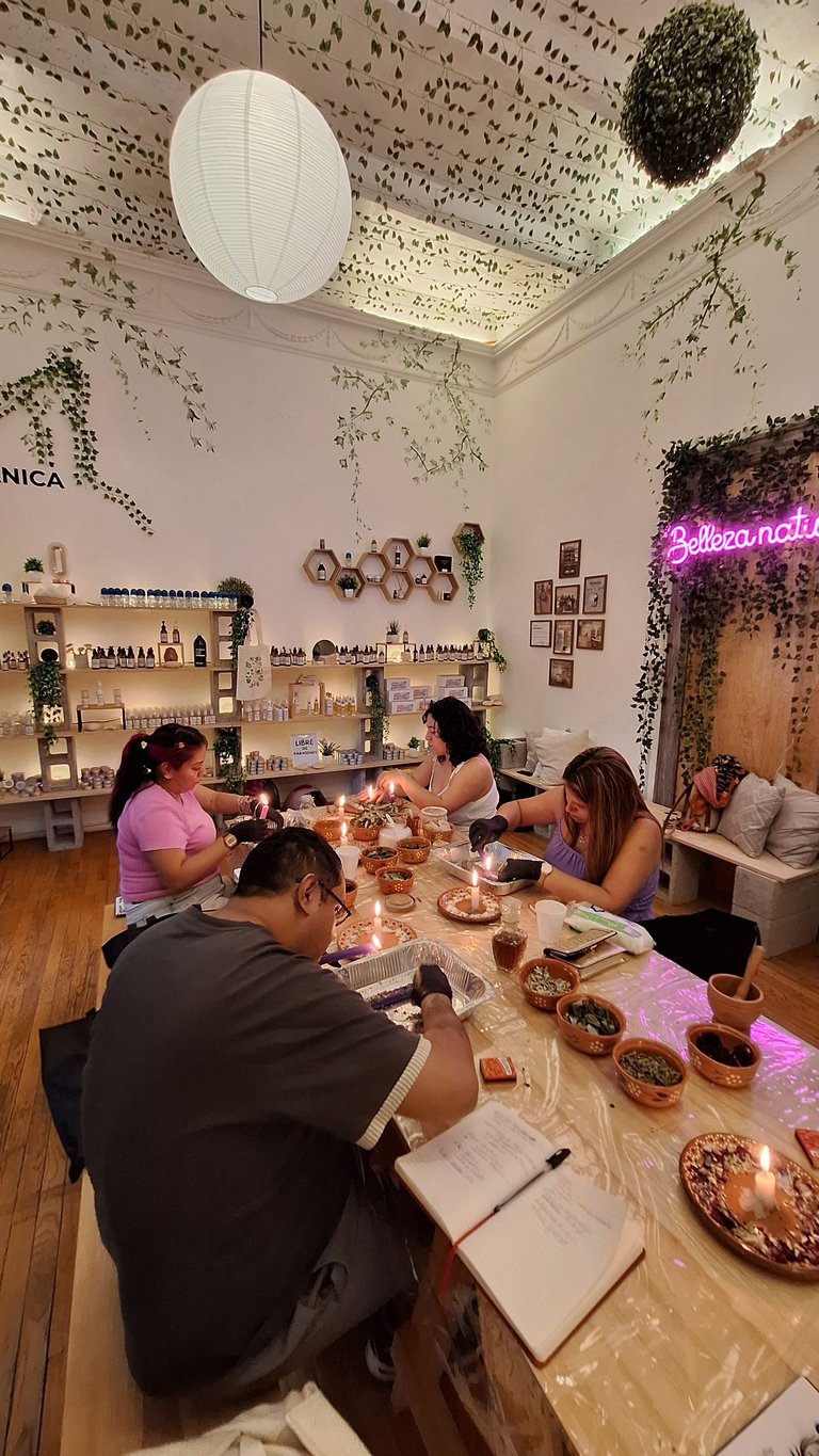 Four women sitting at a table in a nail salon decorated with plants, neon signs, and hanging ivy